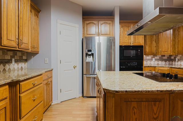 kitchen featuring island exhaust hood, decorative backsplash, light stone countertops, black appliances, and light hardwood / wood-style flooring