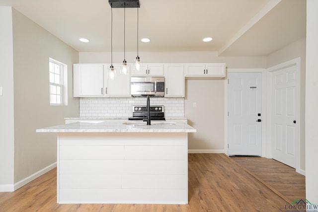 kitchen with sink, white cabinets, hanging light fixtures, a kitchen island with sink, and stainless steel appliances