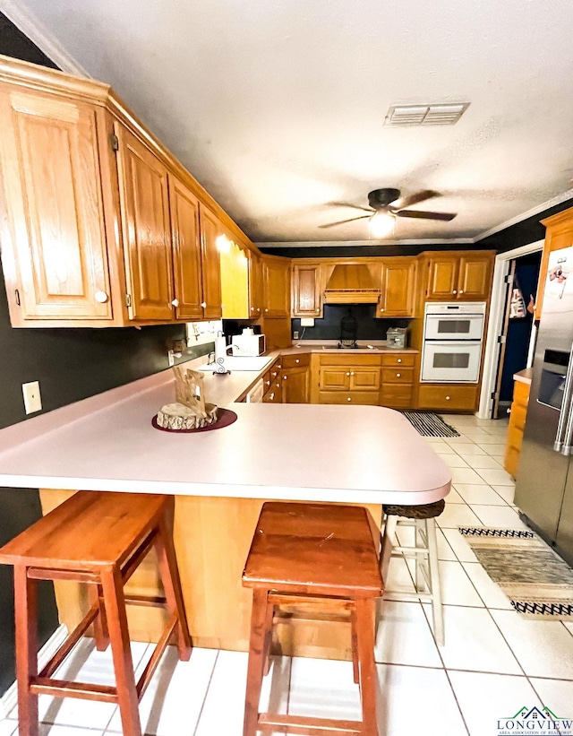 kitchen with kitchen peninsula, a kitchen breakfast bar, double oven, ceiling fan, and light tile patterned floors