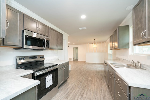 kitchen with pendant lighting, stainless steel appliances, light countertops, a sink, and light wood-type flooring