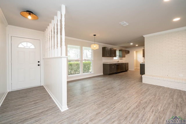 entrance foyer featuring ornamental molding, visible vents, brick wall, and wood finished floors