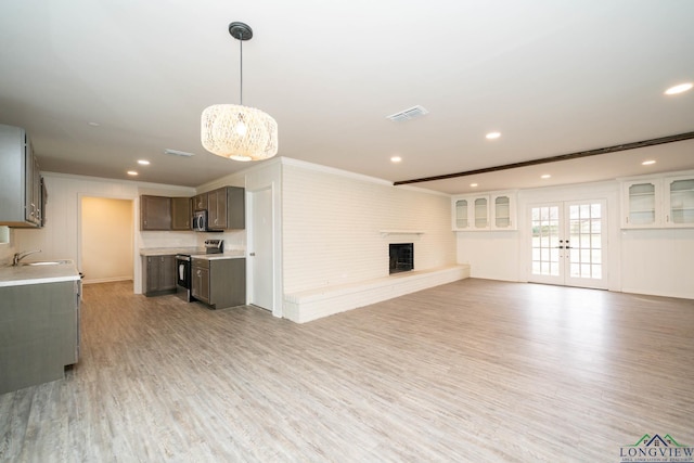 unfurnished living room featuring visible vents, light wood-style flooring, ornamental molding, a large fireplace, and a sink