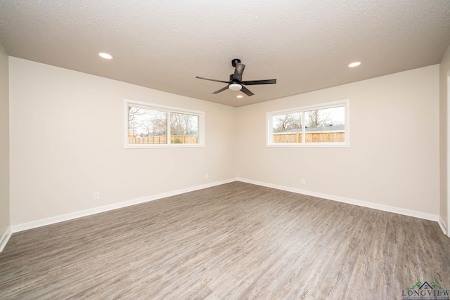 unfurnished room with a textured ceiling, plenty of natural light, wood finished floors, and baseboards