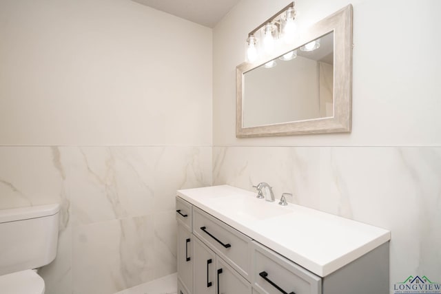 bathroom featuring toilet, vanity, and tile walls