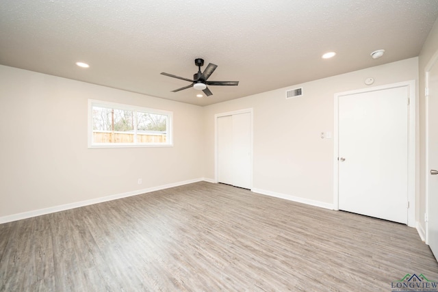 empty room featuring a textured ceiling, light wood finished floors, visible vents, and baseboards