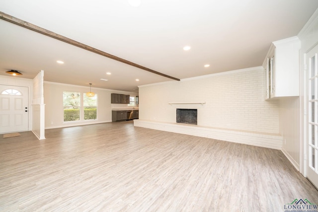 unfurnished living room with a brick fireplace, light wood-style flooring, brick wall, and crown molding