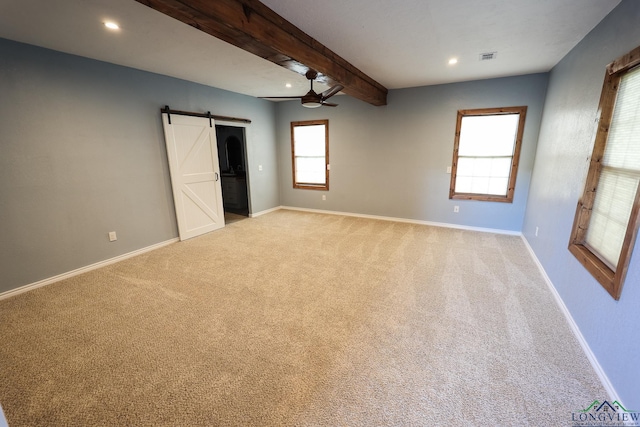 unfurnished bedroom with beamed ceiling, a barn door, light colored carpet, and multiple windows