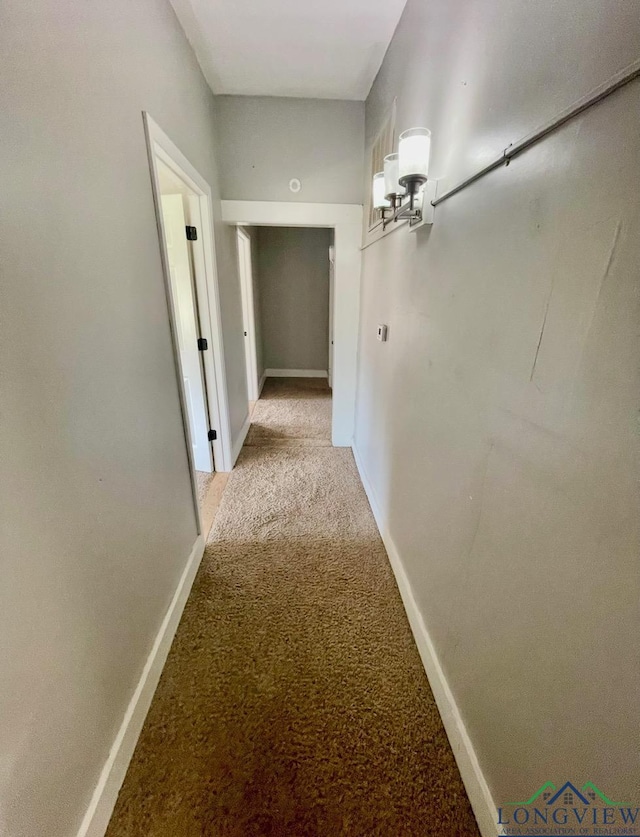 hallway featuring baseboards, light carpet, and an inviting chandelier