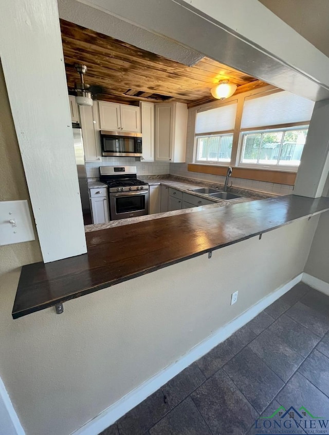 kitchen with white cabinets, appliances with stainless steel finishes, baseboards, wooden ceiling, and a peninsula
