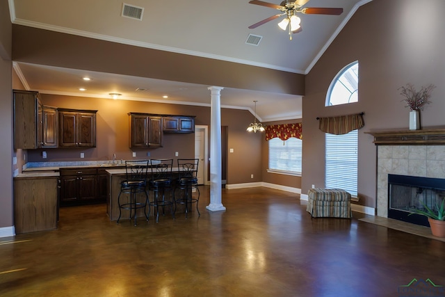 kitchen featuring a center island, ornate columns, a kitchen breakfast bar, ornamental molding, and a tile fireplace