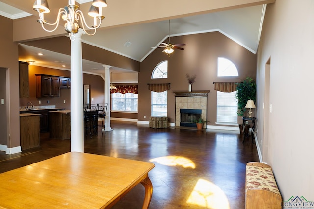 unfurnished living room featuring ornate columns, a fireplace, high vaulted ceiling, ornamental molding, and ceiling fan with notable chandelier