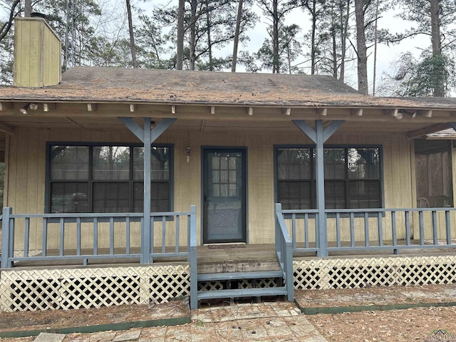 entrance to property with covered porch and roof with shingles