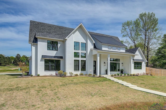 modern farmhouse style home with metal roof, fence, a front lawn, brick siding, and a shingled roof