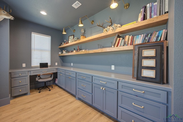 office space featuring built in desk, light wood-type flooring, and visible vents