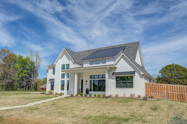 modern inspired farmhouse with metal roof, fence, brick siding, a front lawn, and a standing seam roof