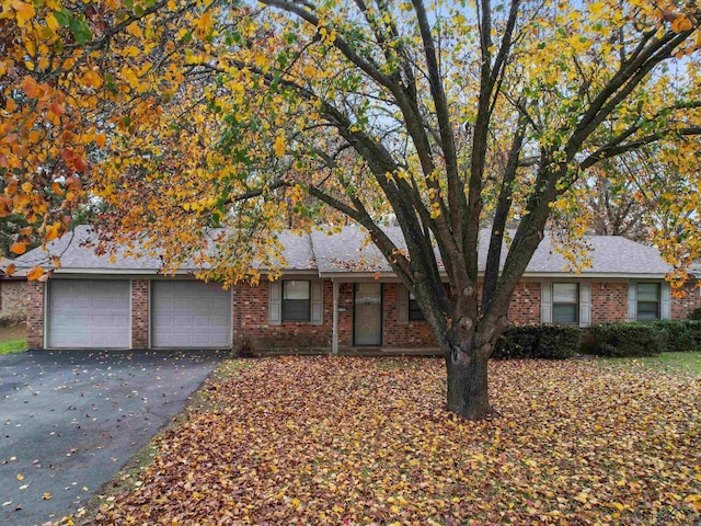 ranch-style house featuring aphalt driveway, brick siding, and a garage