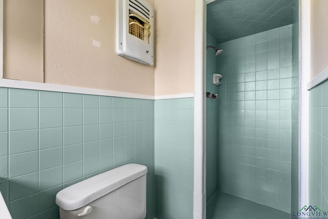 bathroom featuring a wainscoted wall, tile walls, toilet, and a stall shower