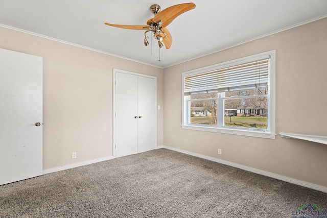 unfurnished bedroom featuring crown molding, baseboards, carpet floors, a closet, and a ceiling fan