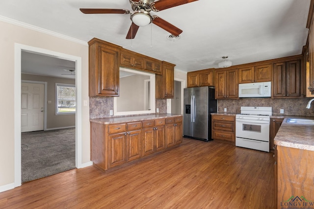 kitchen with decorative backsplash, wood finished floors, white appliances, a ceiling fan, and a sink