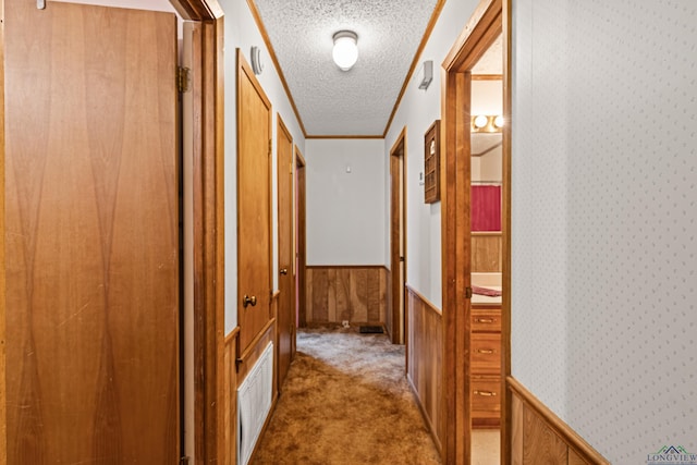 corridor featuring carpet flooring, a textured ceiling, crown molding, and wooden walls