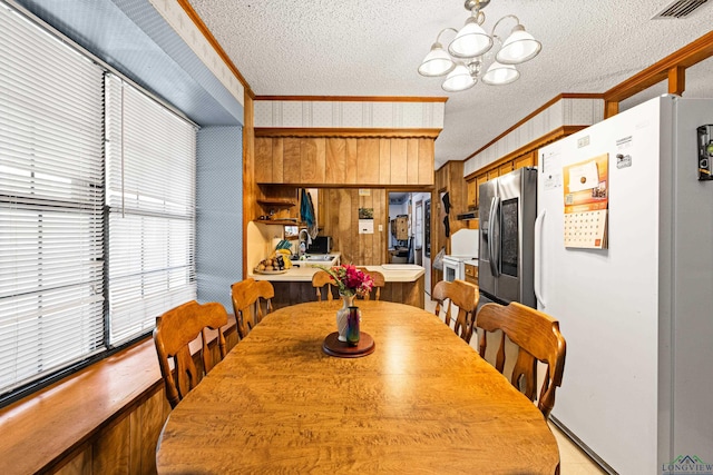 dining space featuring a textured ceiling, wood walls, crown molding, and a chandelier