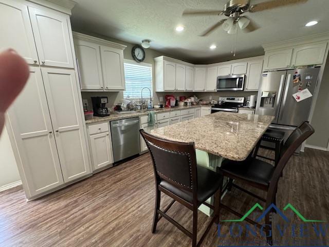 kitchen with appliances with stainless steel finishes, a breakfast bar, white cabinetry, dark hardwood / wood-style floors, and a kitchen island