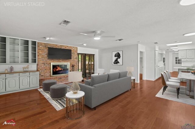 2804 Palm Plz, Marshall, TX 75672 - living room featuring dark wood-style floors, a brick fireplace, a ceiling fan, a textured ceiling, and baseboards