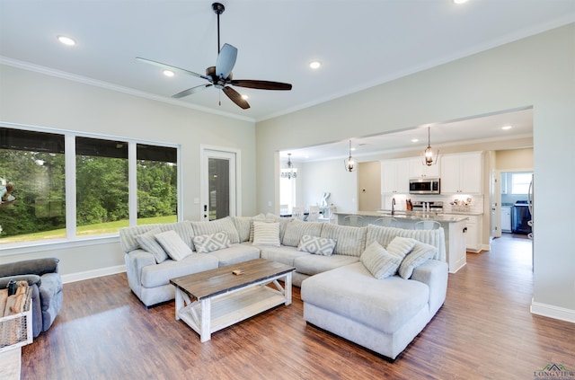 living area with baseboards, recessed lighting, ceiling fan with notable chandelier, wood finished floors, and crown molding
