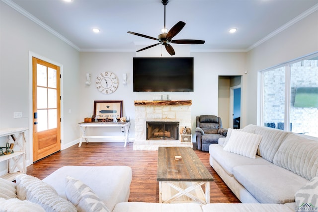 living area featuring a ceiling fan, wood finished floors, a stone fireplace, and crown molding