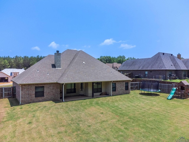 rear view of house with a playground, a patio area, a trampoline, and a lawn