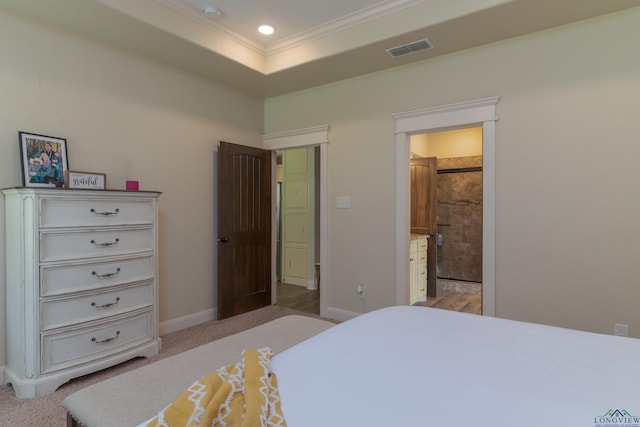 bedroom with a tray ceiling, ensuite bathroom, light colored carpet, and ornamental molding