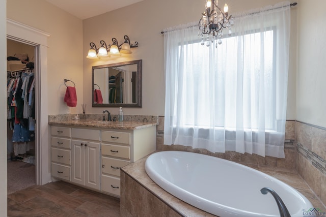 bathroom featuring vanity, tiled tub, and an inviting chandelier