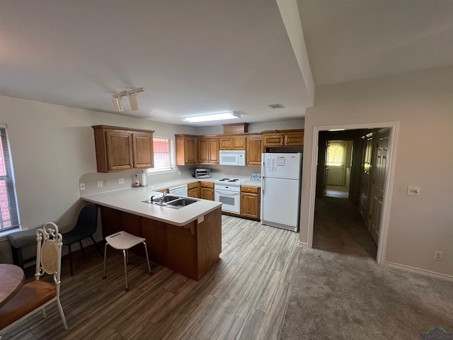 kitchen with kitchen peninsula, light wood-type flooring, white appliances, and a breakfast bar area