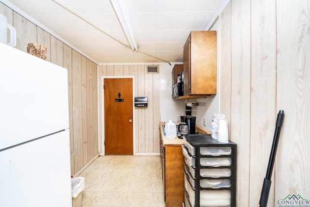 kitchen with light countertops, freestanding refrigerator, visible vents, and wooden walls