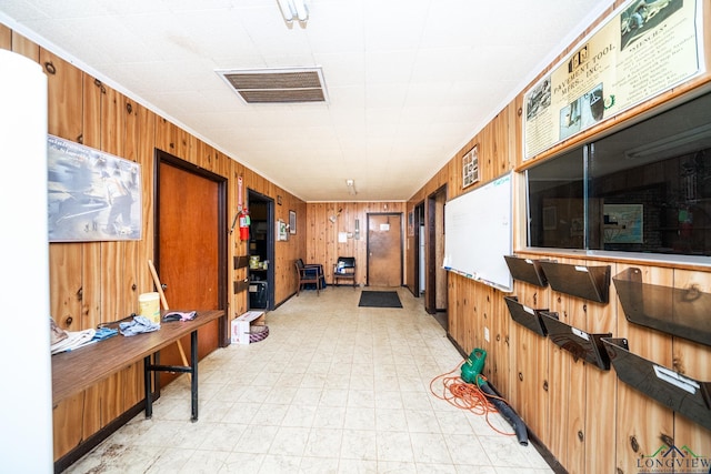 corridor featuring crown molding, visible vents, wood walls, and light floors