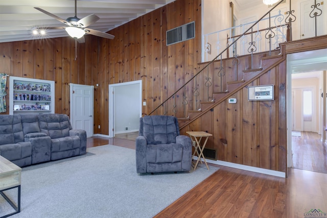 living room featuring ceiling fan, wooden walls, hardwood / wood-style flooring, beamed ceiling, and a high ceiling