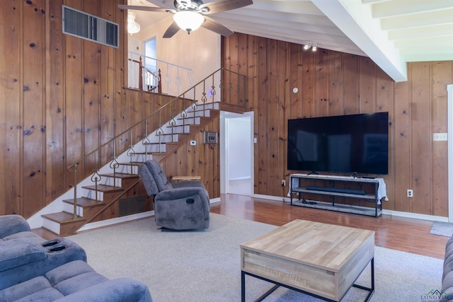 living room with wooden walls, beamed ceiling, wood-type flooring, and ceiling fan