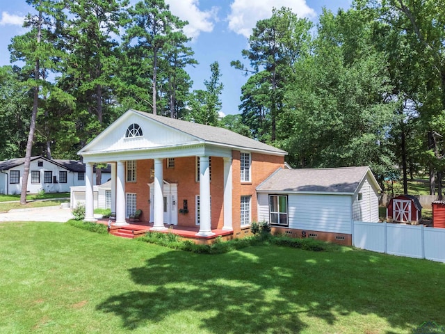 neoclassical home featuring covered porch, an outbuilding, and a front yard