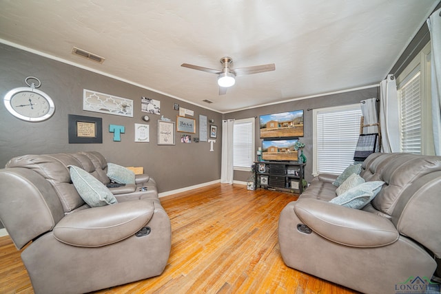 living area with a ceiling fan, visible vents, baseboards, ornamental molding, and light wood-type flooring