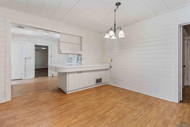 kitchen with kitchen peninsula, pendant lighting, a chandelier, white cabinets, and light wood-type flooring