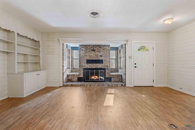 unfurnished living room with a fireplace, light hardwood / wood-style floors, built in features, and wooden walls