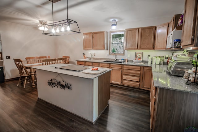 kitchen with cooktop, dark wood-type flooring, sink, pendant lighting, and a kitchen island