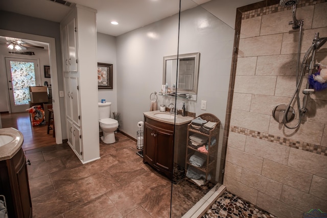 bathroom with vanity, ceiling fan, a tile shower, and toilet