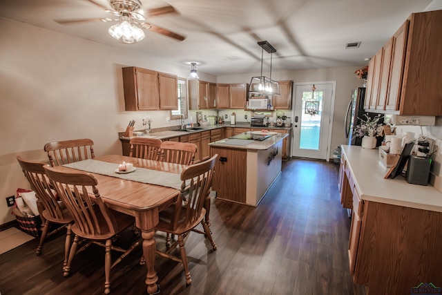 kitchen with stainless steel refrigerator, ceiling fan, a center island, dark hardwood / wood-style flooring, and decorative light fixtures