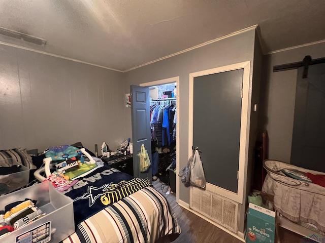 bedroom with a closet, crown molding, wood-type flooring, and a barn door