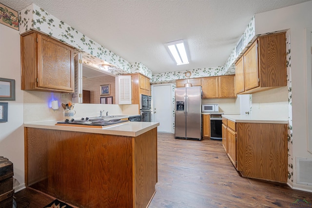 kitchen with kitchen peninsula, hardwood / wood-style floors, a textured ceiling, and appliances with stainless steel finishes