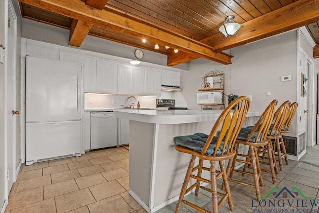 620 Shadywood Ln, Avinger, TX 75630 - kitchen with white appliances, under cabinet range hood, light countertops, white cabinetry, and a breakfast bar