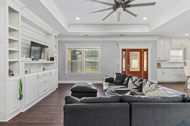 living room with a tray ceiling, ceiling fan, dark wood-type flooring, and ornamental molding