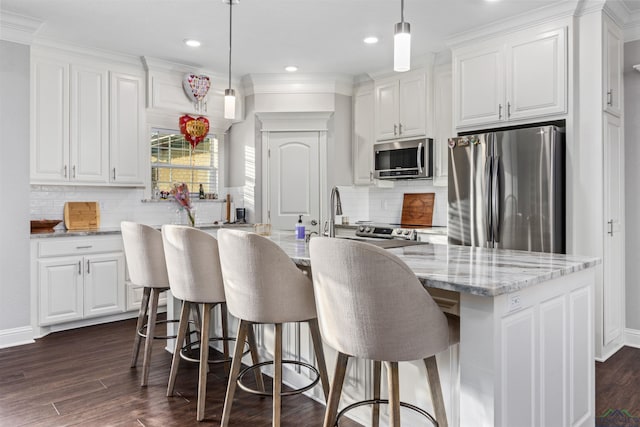 kitchen featuring appliances with stainless steel finishes, light stone counters, pendant lighting, a center island with sink, and white cabinetry