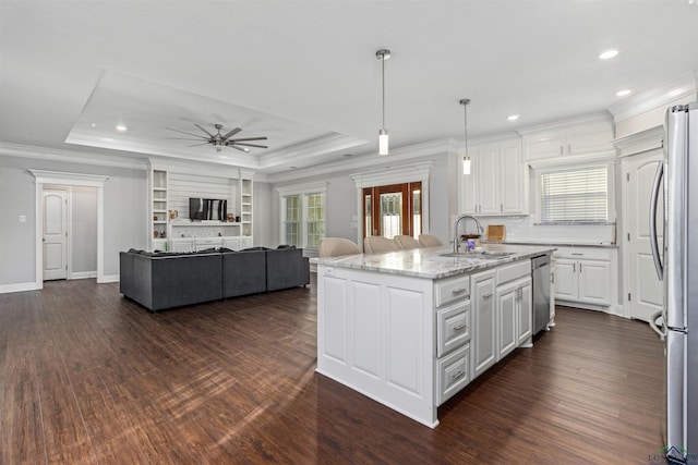 kitchen featuring a tray ceiling, a center island with sink, hanging light fixtures, and appliances with stainless steel finishes